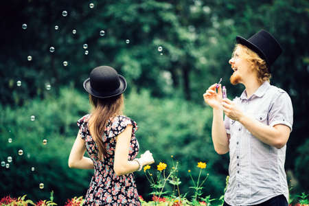 Happy funny hipster couple playing together blowing soap bubbles outdoor in spring park.