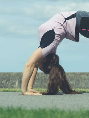 Super fit attractive young woman wearing fashionable outfit working out being active outside during sunny weather. Stretching her back or practice yogaの写真素材