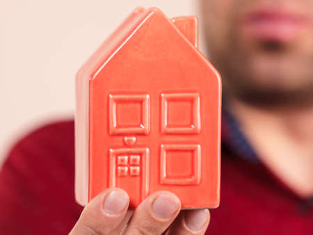Unrecognizable man holding small red house model on palm of hand. Real estate concept.の写真素材