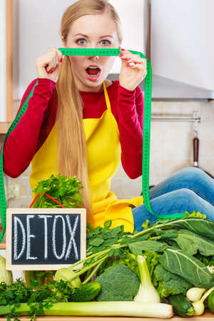 Young woman in kitchen having many green vegetables presenting board with detox sign.の写真素材