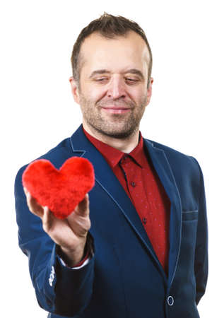 Elegant businessman wearing formal suit holding love symbol, little red heart shaped pillow. Studio shot on isolated background.の写真素材