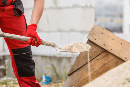 Unrecognizable person worker using shovel standing on industrial construction site, working hard on house renovation.の写真素材