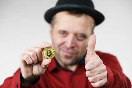 Adult man having bitcoin coin in hand showing thumbs up gesture. Crypto internet currency banking concept.の写真素材