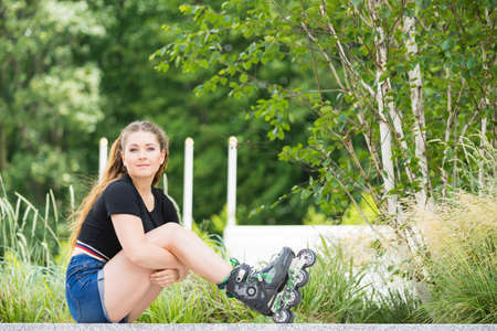 Woman wearing roller skates sitting in park. Female relaxing after a long ride.