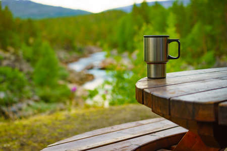 Picnic site table with thermal mug, norwegian mountains nature in the background. Camping with thermos.の写真素材