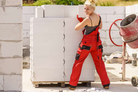 Strong pretty woman working on construction site, building house, installing gray airbricks. Industrial work concept.の写真素材