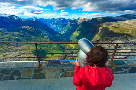 Tourism vacation and travel. Female looking through sightseeing binoculars tourist telescope, overlooking Geirangerfjord and mountains landscape from Dalsnibba viewpoint, Norwayの写真素材