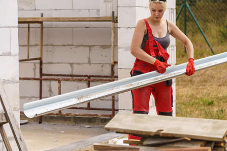 Woman carrying steel metal made gutter on her house construction site, building new home, fixing...