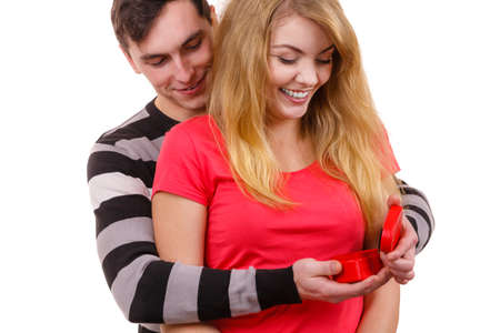 Couple and holiday concept. Handsome man surprising cheerful woman with red heart shaped gift box...