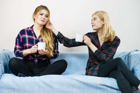 Two women spending time together on sofa drinking tea. Female complaining, the other one comforting her. Perks of friendship.の写真素材