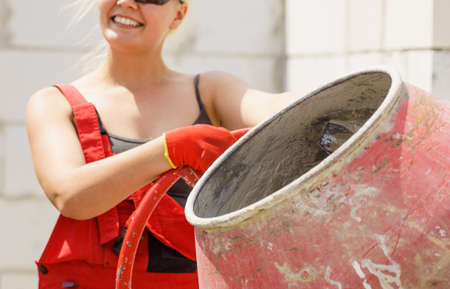 Strong woman worker working with red concrete cement mixer machine on house construction site. Industrial work equipment concept.の写真素材