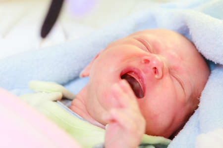 Infant care, teething pain, colic ache concept. Little newborn baby crying in bed surrounded with blanketsの写真素材