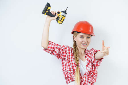 Woman wearing helmet using drill. Girl working at flat remodeling. Building, repair and renovation.の写真素材