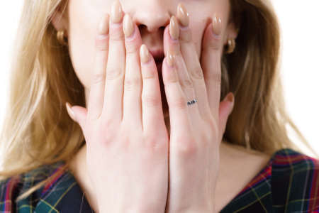 Close up of young blonde woman showing silence gesture hiding her mouth being hands.の写真素材