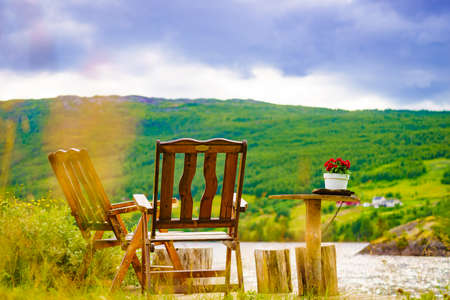 Picnic site rest stop area wooden table with flowers decoration and chairs on norwegian lake fjord shore. Holidays relaxation on trip. Scandinavia Europe.の写真素材