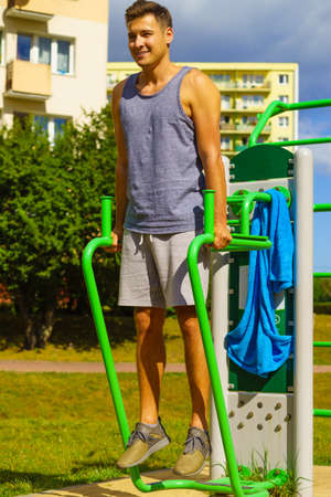 Young handsome man working out in outdoor gym. Sporty guy flexing his muscles doing sit ups on...