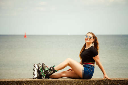 Happy joyful young woman wearing roller skates relaxing after long ride. Female being sporty having fun during summer time near sea.の写真素材