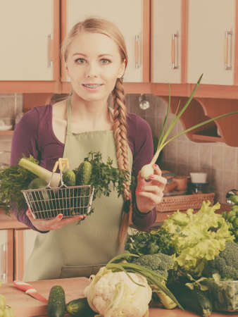 Buying healthy dieting food concept. Woman in kitchen having many green vegetables holding small shopping basket trolley.の写真素材
