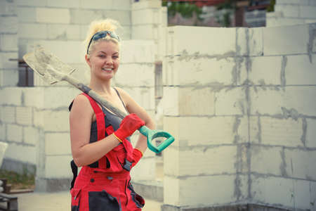 Woman worker using shovel standing on industrial construction site, working hard on house renovation.の写真素材