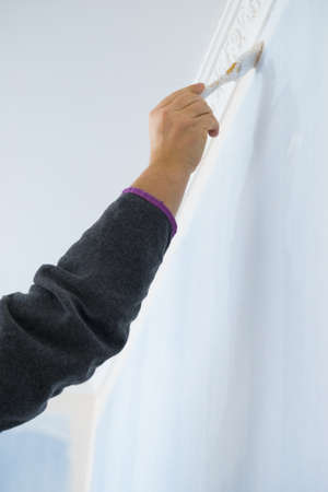 Person appplying white paint on blue wall using brush. Home renovation concept.の写真素材