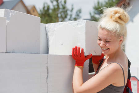 Strong pretty woman working on construction site, building house, installing gray airbricks. Industrial work concept.の写真素材