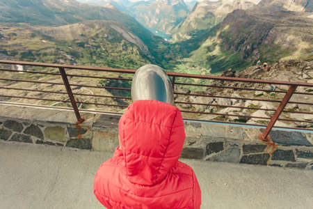 Tourism vacation and travel. Female looking through sightseeing binoculars tourist telescope, overlooking Geirangerfjord and mountains landscape from Dalsnibba viewpoint, Norwayの写真素材