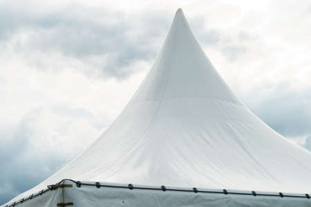 Spiked roof of white party event tent against sky with dark clouds.の写真素材