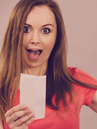 Shocked amazed woman with brown long hair holding small piece of paper, shopping list, receipt, bill of sale looking amazed.の写真素材