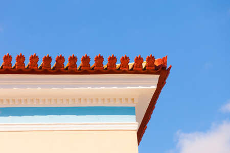 Old fashioned decorative red elements on edge of roof light colored building home against sky.