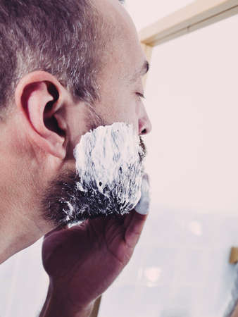 Man preparing his facial hair before trimming his beard, applying shaving cream foam mousse. Male beauty treatment concept.の写真素材