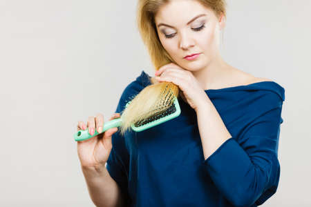 Woman combing her hair with brush. Young female with beautiful natural blond straight long hairs, studio shot on greyの写真素材