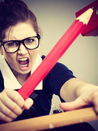 Mobbing at work, bad job relations concept. Angry mad bossy businesswoman being furious sitting working at desk full off documents in binders.の写真素材