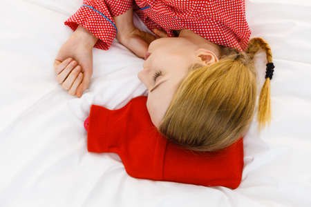 Woman lying on bed sleeping with warm red hot water bottle. Fever, flu treatment objects concept.の写真素材