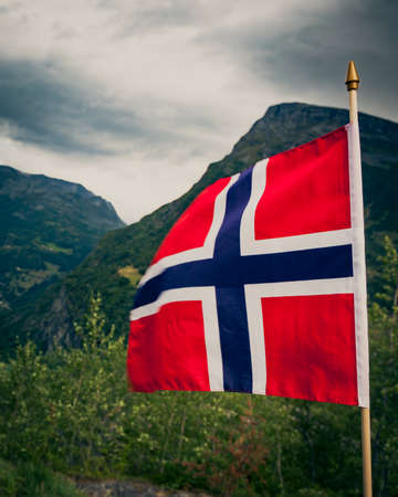 The norwegian flag waving against green mountains
