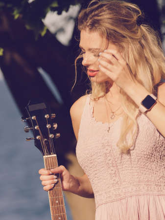 Hippie looking young adult woman wearing gypsy outfit having acoustic guitar. Female playing music in park.の写真素材