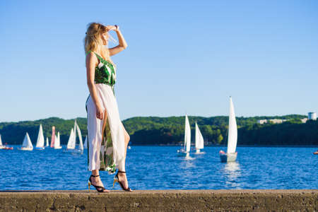 Beautiful fashion model against sea. Pretty blonde young adult woman wearing long white green summer dress.の写真素材