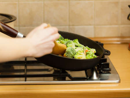 Woman in kitchen cooking stir fry frozen vegetables on pan and tasting. Girl frying making delicious dinner food meal.の写真素材