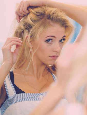 Woman looking at herself in bathroom mirror fixing her look, adding finish touch.の写真素材