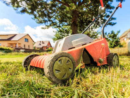 Gardening, garden service. Old lawn mower cutting green grass in backyard. Mowing field with...