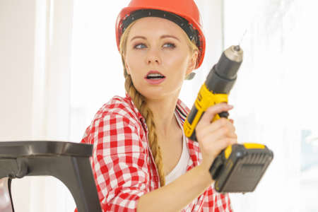 Woman wearing helmet using drill. Girl working at flat remodeling. Building, repair and renovation.の写真素材