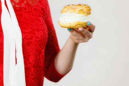 Unrecognizable woman hand holding choux puff with cream flavour. Unhealthy eating, sweet baked food...