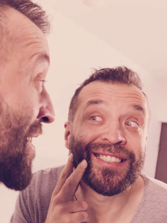 Mature adult man investigating his unshaved facial hair. Guy thinking about shaving his short beardの写真素材