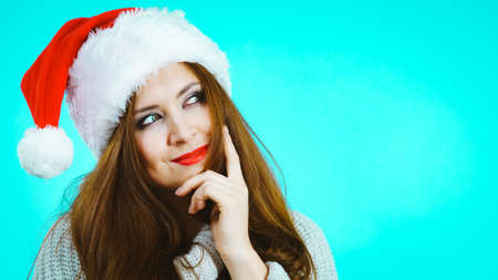 Santa Claus girl in red hat having idea for Christmas gift. Female in festive headwear on blue background.の写真素材