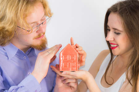 Happy young couple is ready to live together. Man and woman holding small red house model. Home ownership, real estate concept.の写真素材