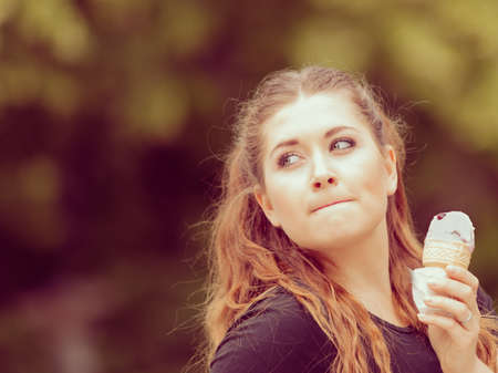 Happy funny young woman with long brown hair eating ice cream having fun enjoying her dessert during...