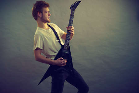 Young bearded man with electric guitar. Adult person is holding instrument and playing. Hobby, music...