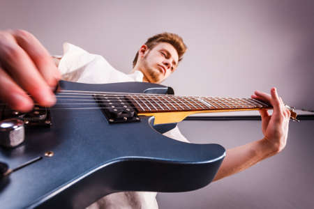 Young bearded man with electric guitar. Adult person is holding instrument and playing. Hobby, music concept, on greyの写真素材