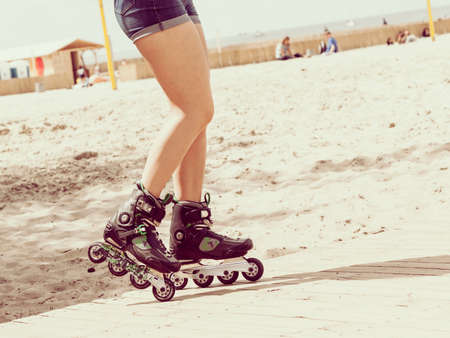 Woman legs wearing roller skates riding on beach. Female being sporty having fun during summer time.