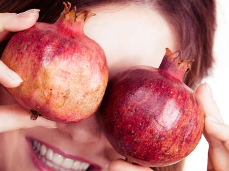 Joyful young woman playing with pomegranate fruits, close up Healthy eating, cancer prevention, immune support concept.の写真素材