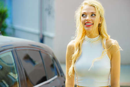 Woman having funny face expression standing next to auto being afraid to drive car.